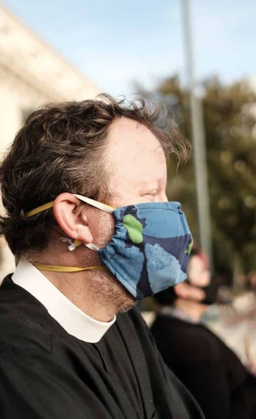 man in clergy collar wearing mask at protest